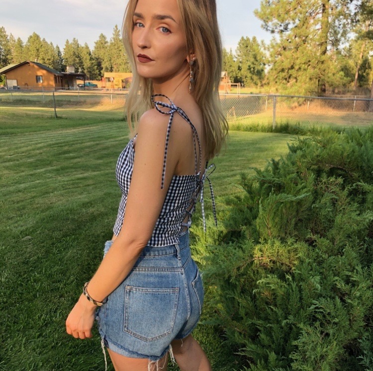 back view of white woman with blonde hair wearing a gingham crop top that laces up and denim shorts
